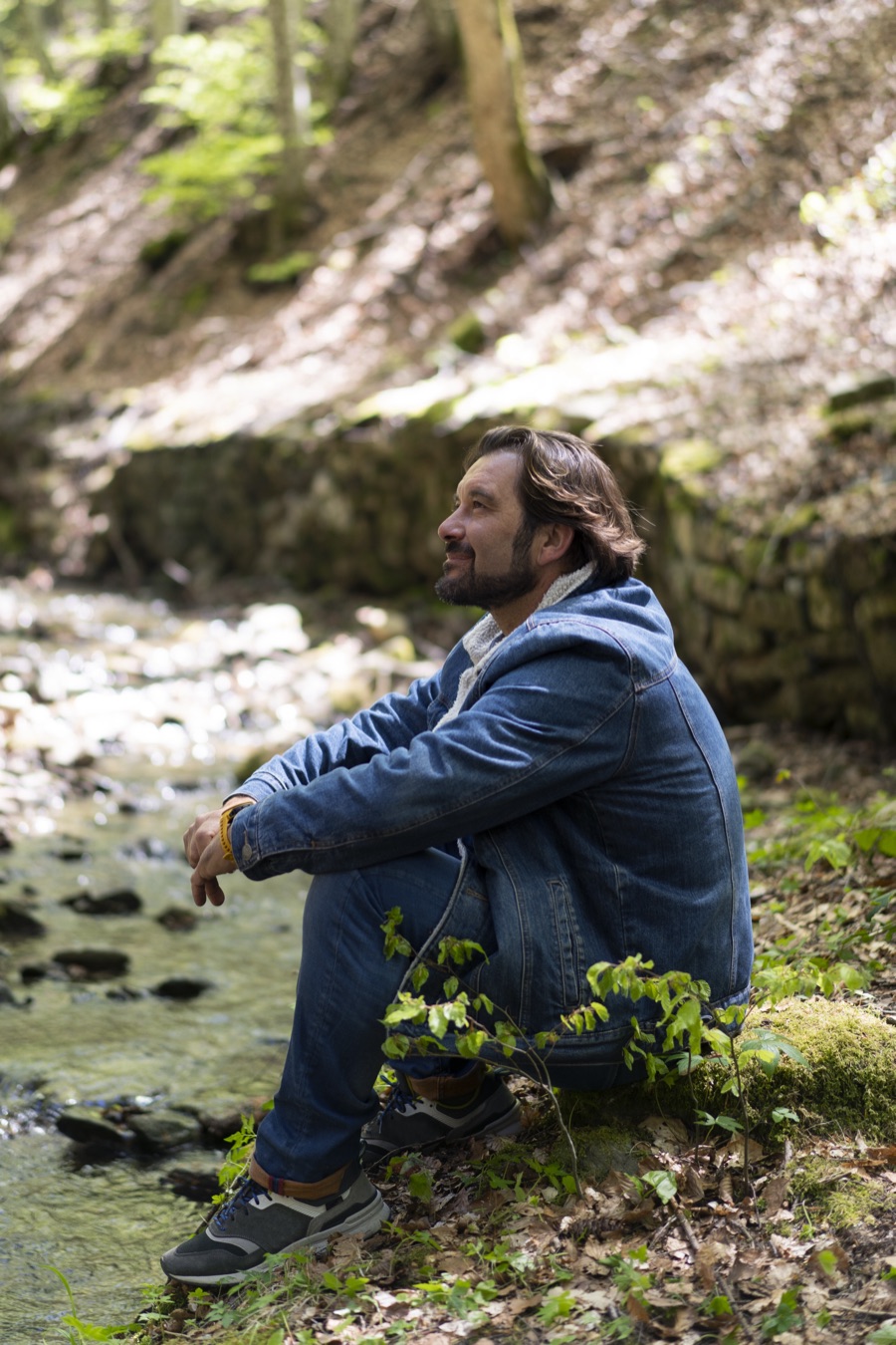 Man sitting quietly by a woodland stream, taking a reflective moment outdoors